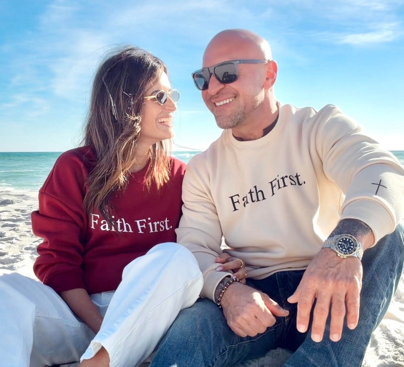 Two people sitting on a beach with 'Faith First' shirts.